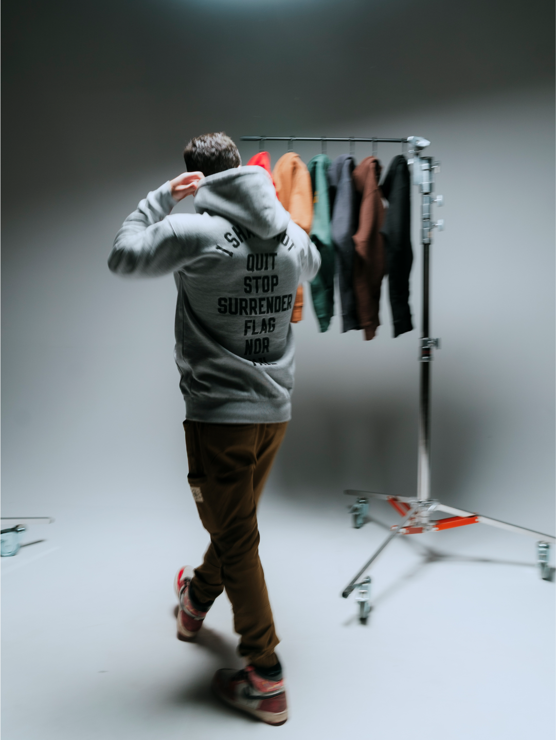 a motion blurred photo of a man walking through a studio shot of a row of anthem hoodies on hangars.