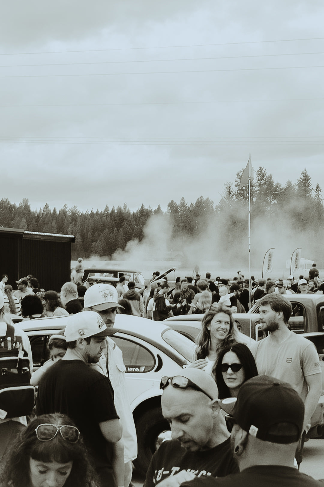 Crowd of people at an outdoor event with tire smoke in the background