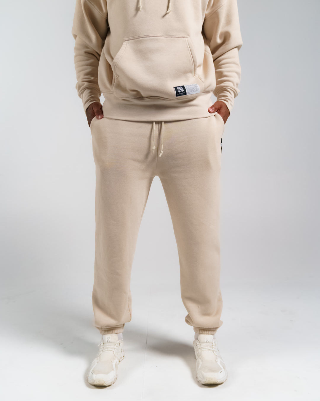 Person wearing a cream hoodie and jogger set on a white background
