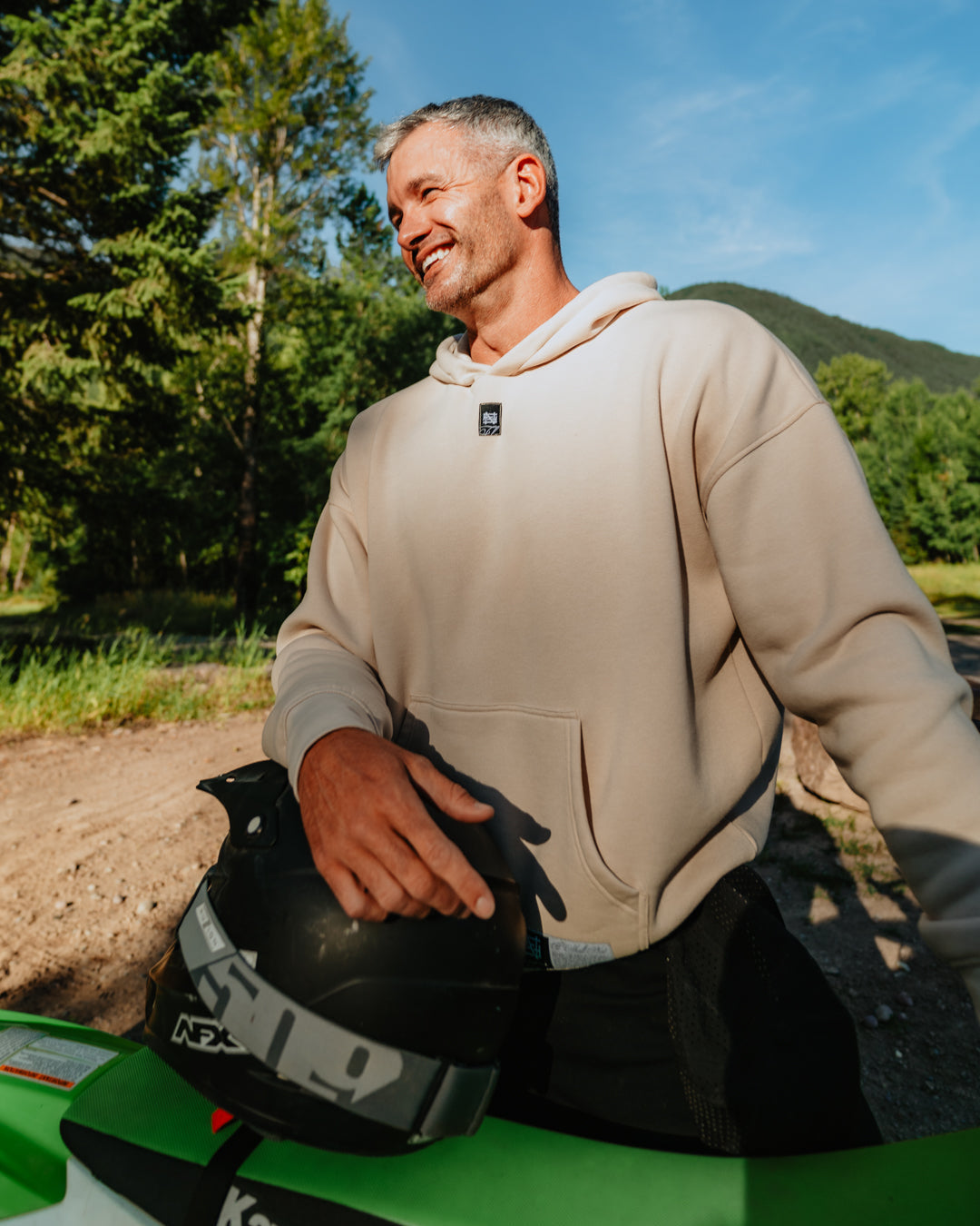 Man holding a helmet next to a green Kawasaki ATV with a scenic background