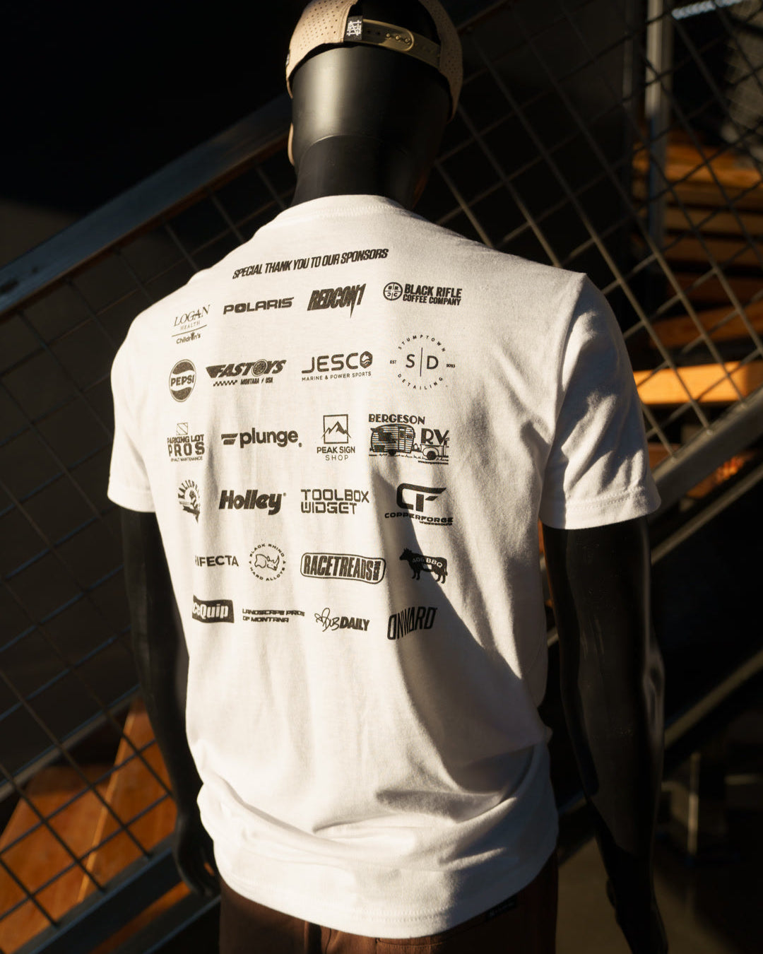 Mannequin wearing a white t-shirt with multiple brand logos against a dark background