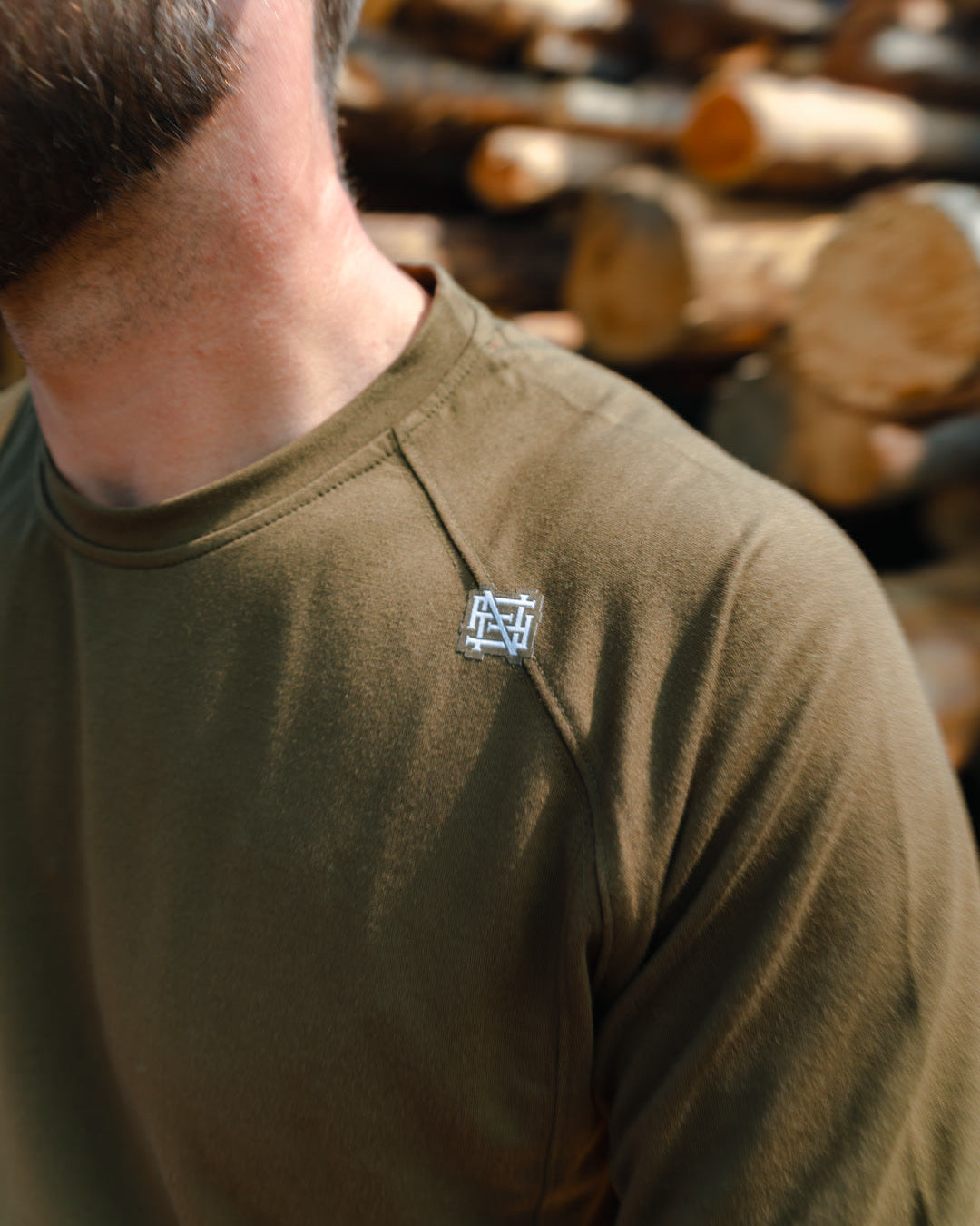 Man wearing a green t-shirt with a logo in front of stacked logs