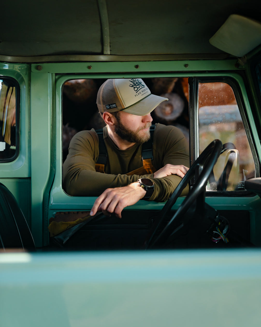 Man leaning inside a window of a vintage green truck wearing a cap and looking sideways.