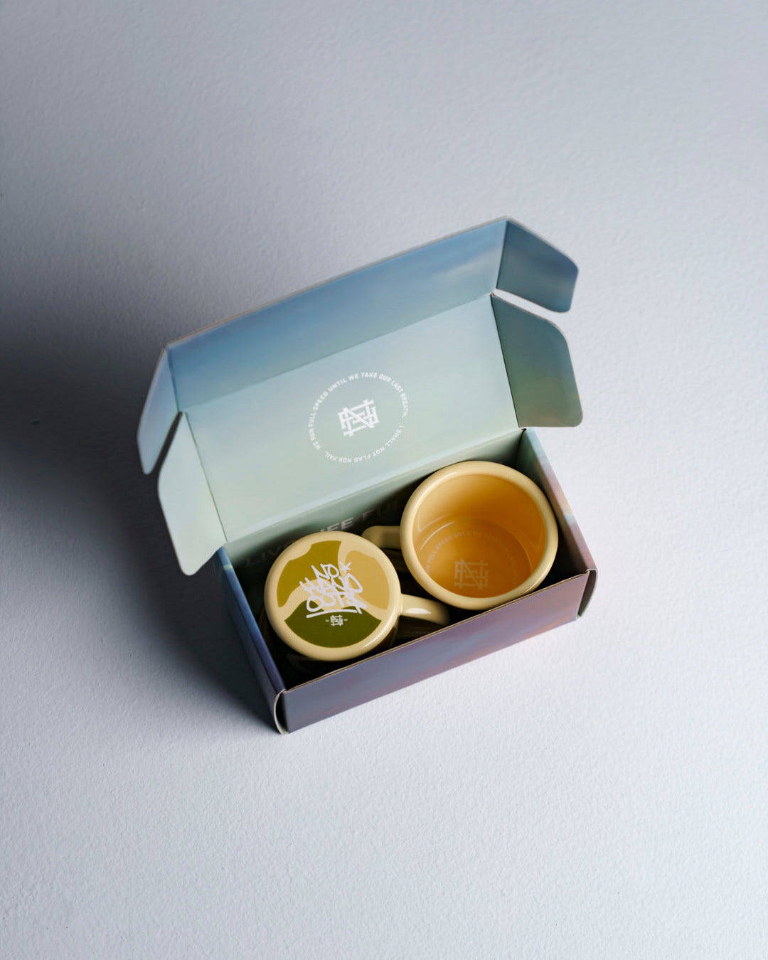 Open box with 2 enamel mugs against studio background
