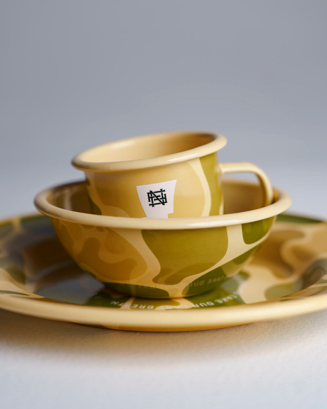 A set of camo-patterned enamelware stacked on top of each other, sitting against studio backdrop