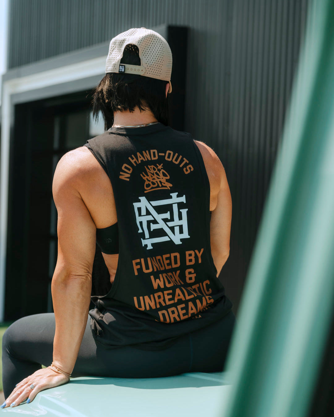 Person wearing a black tank top with text and graphics, sitting on a car.